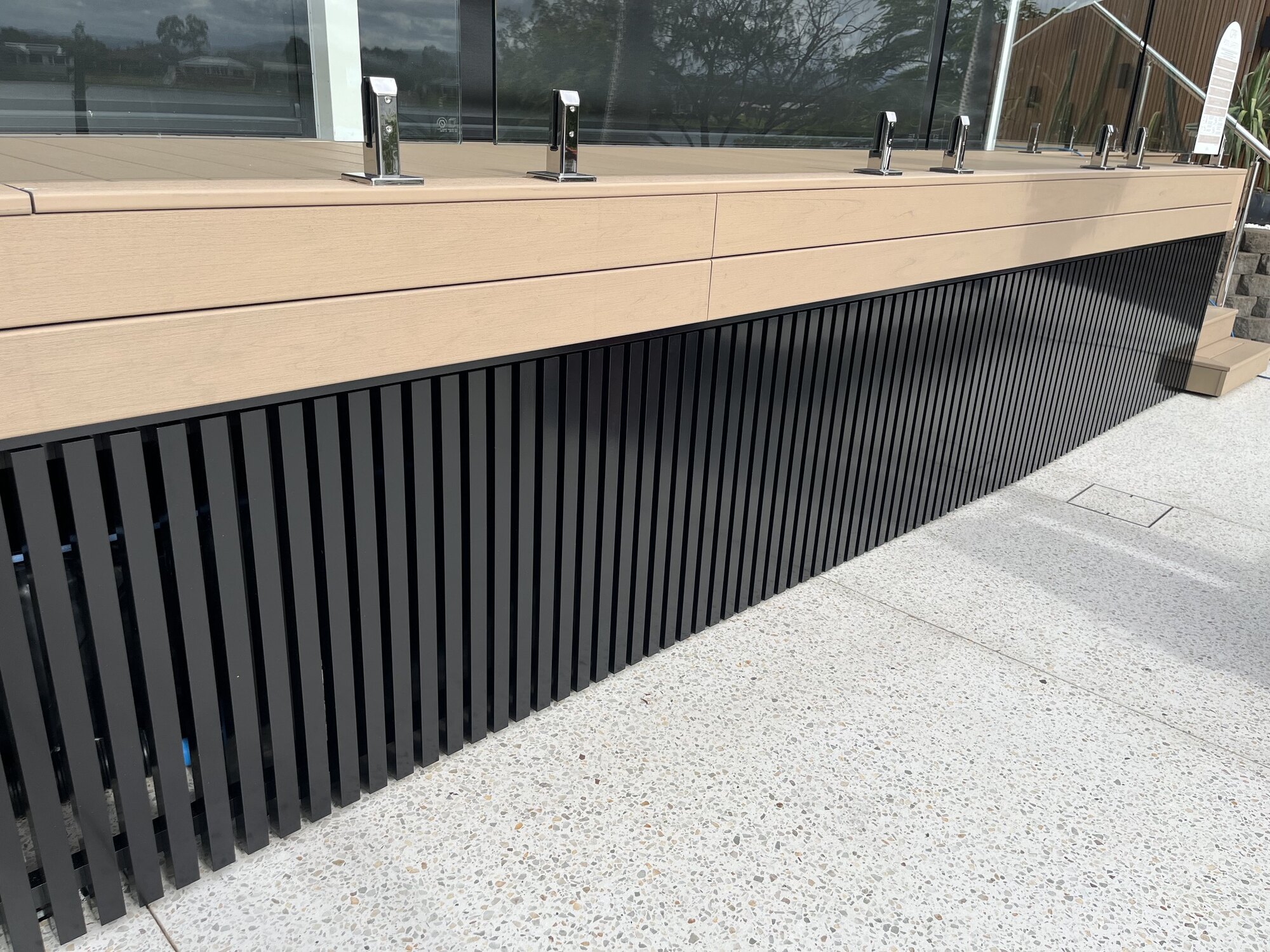 Black aluminium slat screening under a deck with glass balustrade